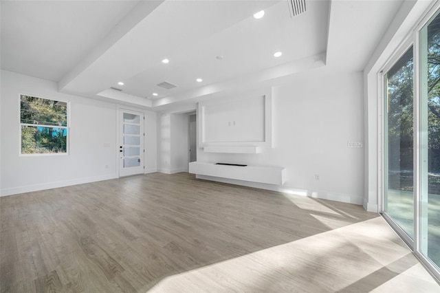 unfurnished living room featuring light wood-type flooring, a wealth of natural light, and a tray ceiling