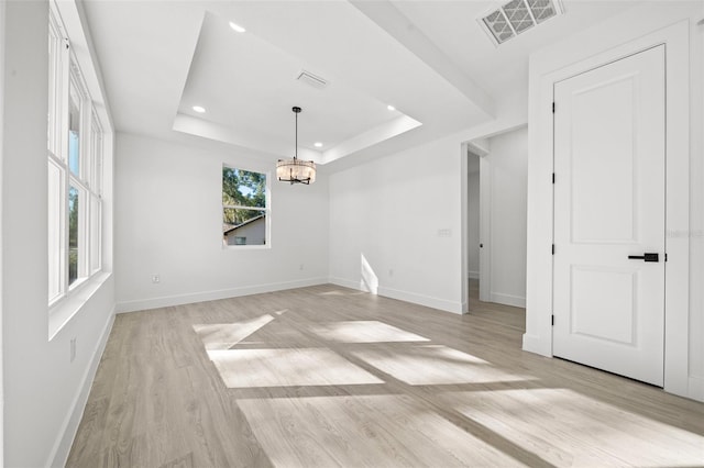 unfurnished dining area featuring light hardwood / wood-style floors, a raised ceiling, plenty of natural light, and a notable chandelier