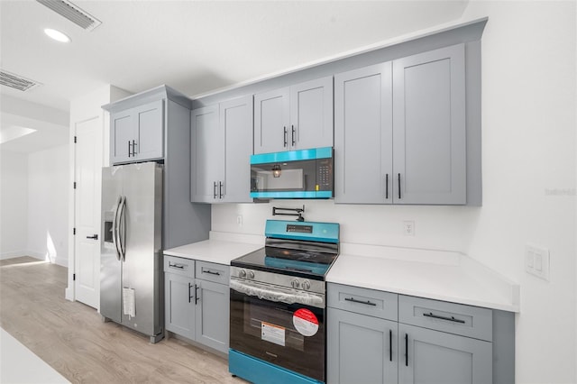 kitchen with gray cabinets, light hardwood / wood-style flooring, and appliances with stainless steel finishes