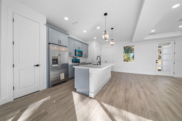 kitchen with appliances with stainless steel finishes, decorative light fixtures, light hardwood / wood-style flooring, and an island with sink