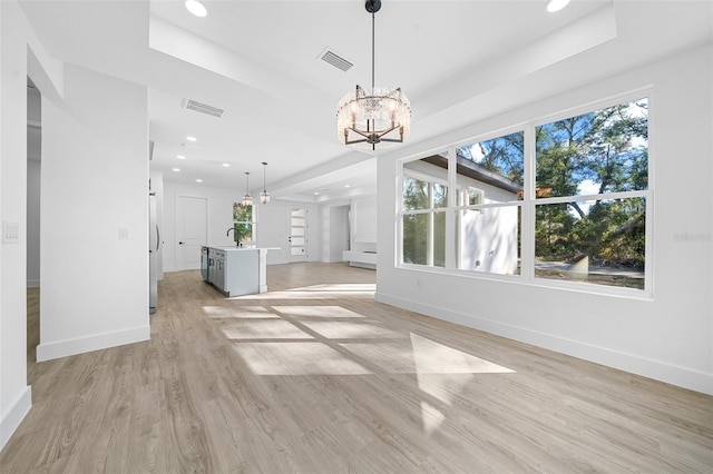 unfurnished living room featuring a wealth of natural light, sink, a notable chandelier, and light wood-type flooring