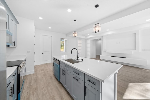 kitchen featuring sink, stainless steel appliances, decorative light fixtures, a kitchen island with sink, and light wood-type flooring