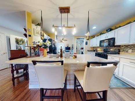 kitchen featuring a kitchen breakfast bar, white cabinetry, pendant lighting, and black appliances