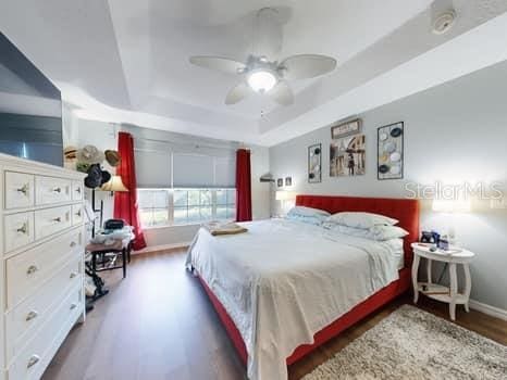 bedroom with ceiling fan, dark hardwood / wood-style flooring, and a tray ceiling