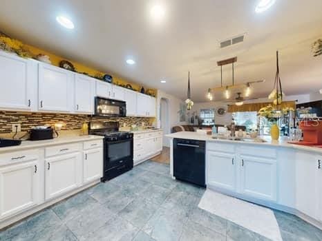 kitchen with kitchen peninsula, backsplash, black appliances, white cabinetry, and hanging light fixtures