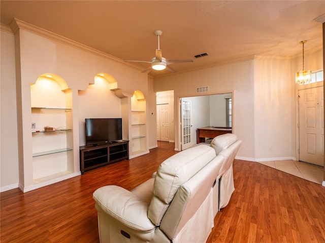 living room featuring wood-type flooring, ceiling fan with notable chandelier, crown molding, and built in shelves