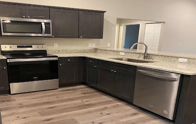 kitchen with sink, light stone countertops, light hardwood / wood-style floors, kitchen peninsula, and stainless steel appliances