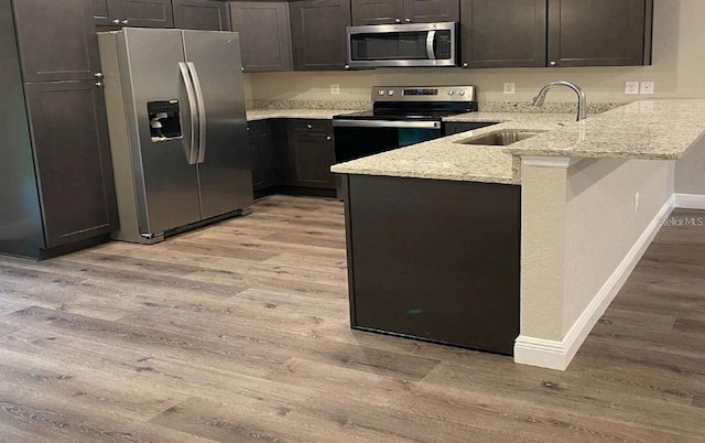 kitchen featuring kitchen peninsula, stainless steel appliances, light stone counters, and light hardwood / wood-style flooring