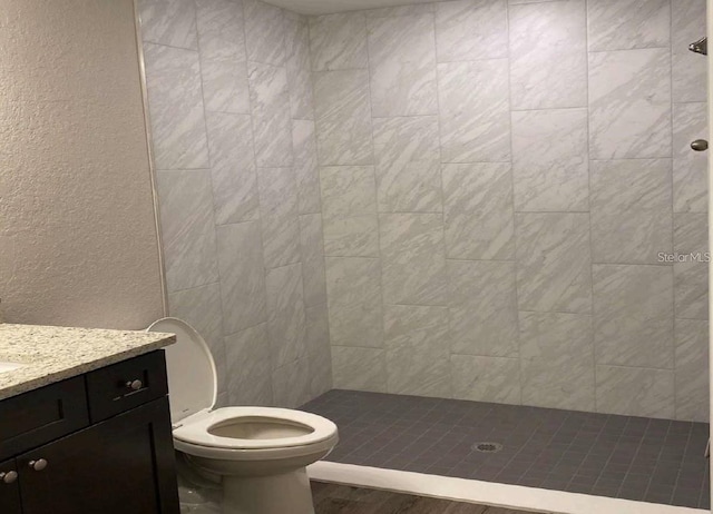 bathroom with a tile shower, vanity, and toilet