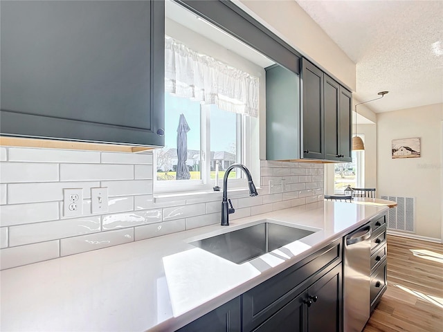 kitchen with sink, stainless steel dishwasher, light wood-type flooring, a textured ceiling, and tasteful backsplash