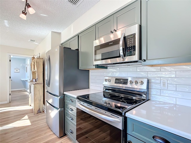 kitchen with gray cabinetry, stainless steel appliances, tasteful backsplash, light hardwood / wood-style flooring, and a textured ceiling