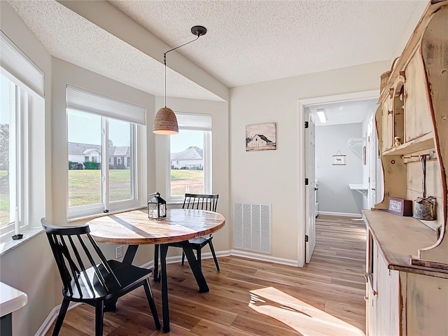 dining space with a textured ceiling, light hardwood / wood-style flooring, and a healthy amount of sunlight