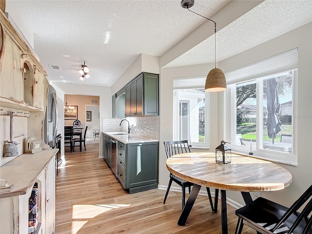 kitchen featuring sink, light hardwood / wood-style flooring, a textured ceiling, decorative light fixtures, and decorative backsplash