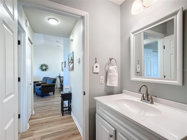 bathroom featuring hardwood / wood-style floors, vanity, lofted ceiling, and a textured ceiling