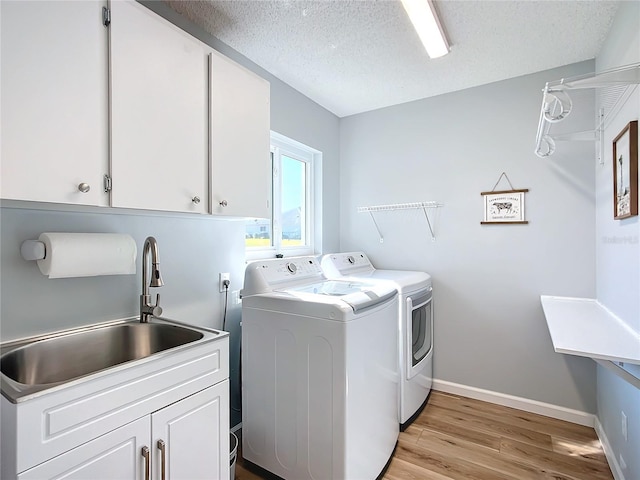 washroom with cabinets, a textured ceiling, sink, washing machine and clothes dryer, and light hardwood / wood-style floors