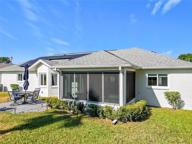 back of house featuring a patio area, a sunroom, a yard, and solar panels