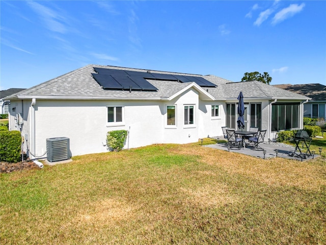 back of property featuring a lawn, a sunroom, solar panels, central AC unit, and a patio