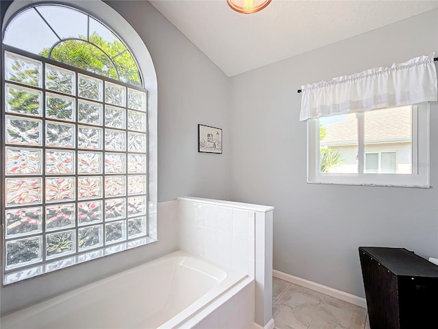 bathroom featuring a relaxing tiled tub and vaulted ceiling