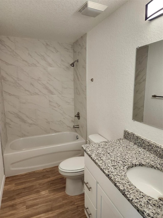 full bathroom with hardwood / wood-style flooring, tiled shower / bath combo, toilet, and a textured ceiling