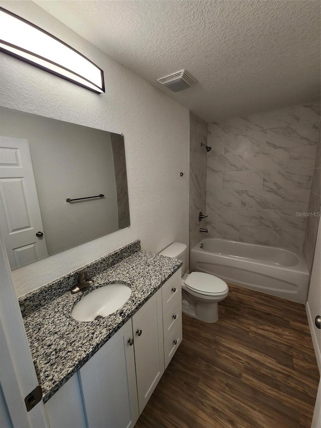 full bathroom featuring tiled shower / bath combo, wood-type flooring, a textured ceiling, toilet, and vanity