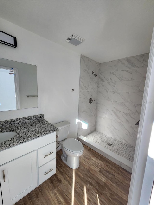 bathroom with a tile shower, hardwood / wood-style floors, vanity, and toilet