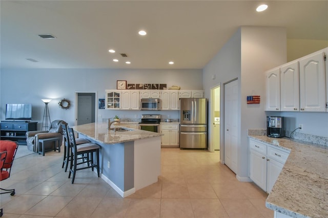 kitchen with white cabinetry, sink, light stone countertops, stainless steel appliances, and a kitchen island with sink