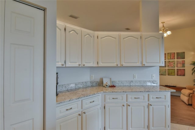 kitchen with light stone countertops, white cabinets, and an inviting chandelier