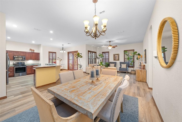 dining space with ceiling fan with notable chandelier and light hardwood / wood-style flooring