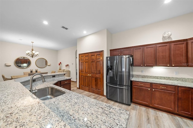 kitchen featuring sink, stainless steel refrigerator with ice dispenser, light stone countertops, light hardwood / wood-style floors, and a chandelier