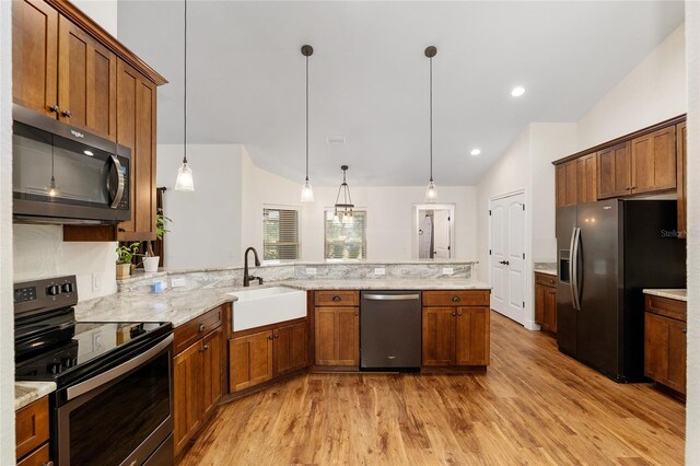 kitchen featuring light stone countertops, stainless steel appliances, sink, decorative light fixtures, and light hardwood / wood-style flooring