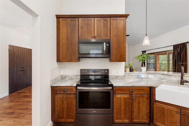 kitchen with light stone countertops, sink, stainless steel appliances, decorative light fixtures, and hardwood / wood-style flooring