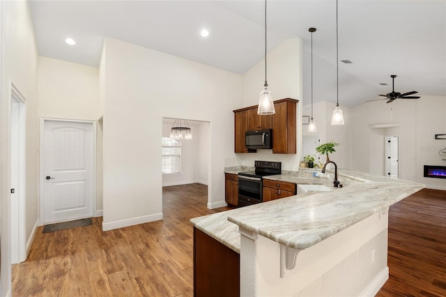 kitchen with a kitchen breakfast bar, light wood-type flooring, sink, black appliances, and decorative light fixtures