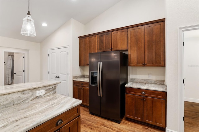 kitchen featuring stainless steel fridge, light stone countertops, light wood-type flooring, and vaulted ceiling