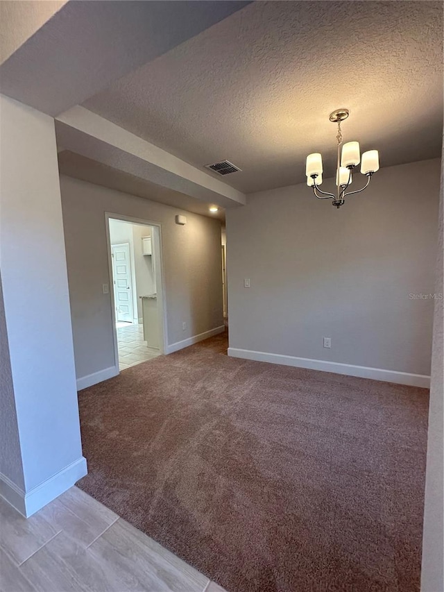 carpeted spare room featuring a textured ceiling and an inviting chandelier