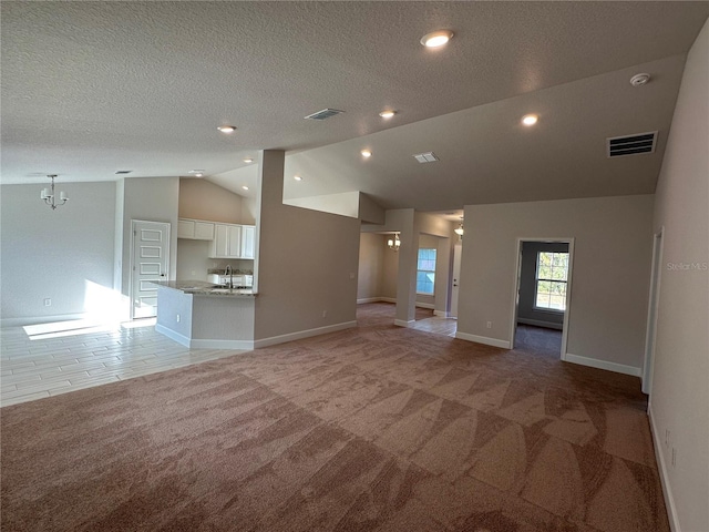 unfurnished living room featuring a textured ceiling, light colored carpet, vaulted ceiling, sink, and an inviting chandelier