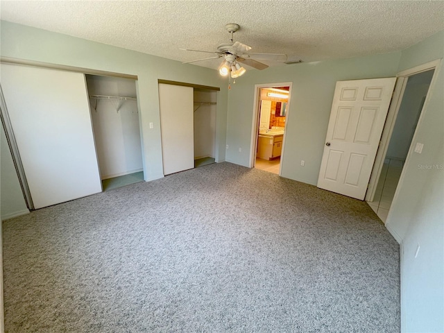 unfurnished bedroom featuring ceiling fan, two closets, a textured ceiling, and ensuite bath