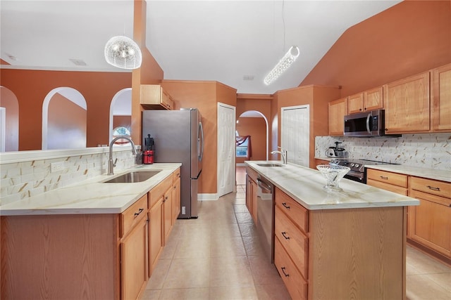 kitchen featuring a center island with sink, sink, vaulted ceiling, decorative light fixtures, and stainless steel appliances