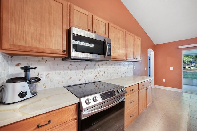 kitchen featuring light stone countertops, appliances with stainless steel finishes, tasteful backsplash, vaulted ceiling, and light tile patterned floors