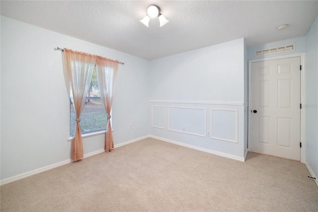 spare room featuring light colored carpet and a textured ceiling