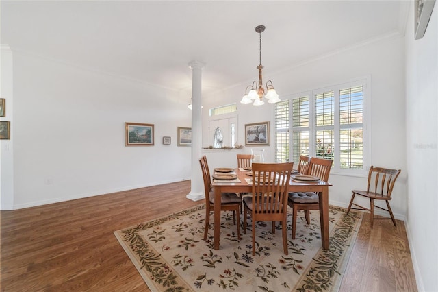 dining room featuring wood-type flooring, an inviting chandelier, crown molding, and ornate columns