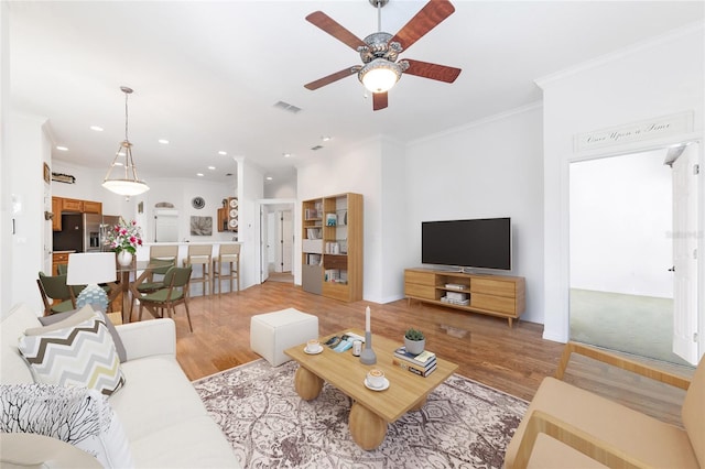 living room featuring wood-type flooring, ceiling fan, and crown molding