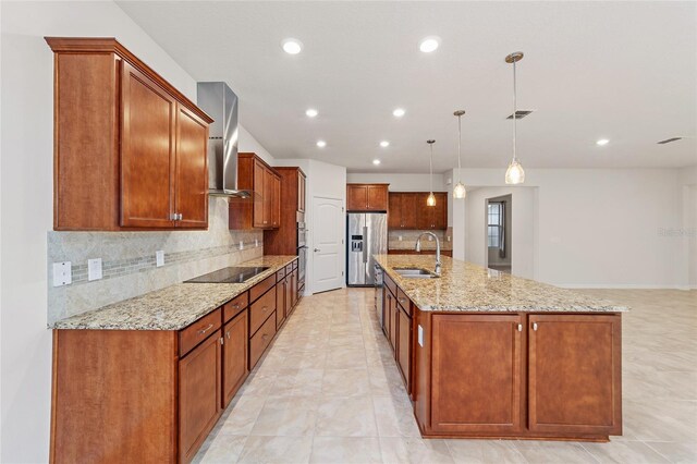 kitchen with a large island with sink, wall chimney range hood, sink, black electric cooktop, and decorative light fixtures