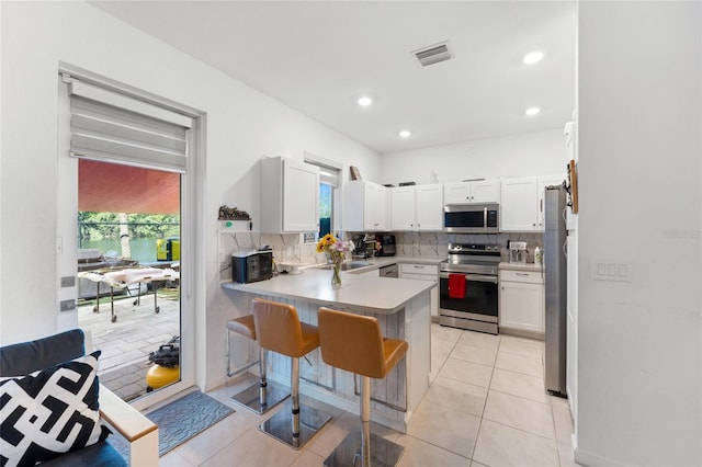 kitchen with visible vents, a peninsula, stainless steel appliances, a kitchen bar, and white cabinetry