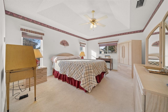 bedroom featuring a textured ceiling, ceiling fan, a raised ceiling, and light carpet