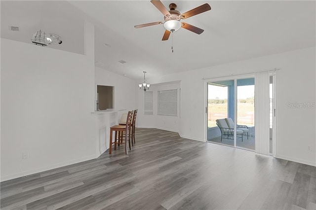 unfurnished living room featuring wood-type flooring, ceiling fan with notable chandelier, and vaulted ceiling