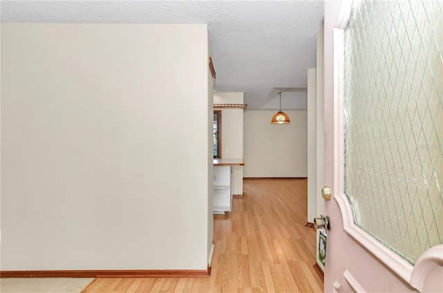 corridor with a textured ceiling and light hardwood / wood-style floors