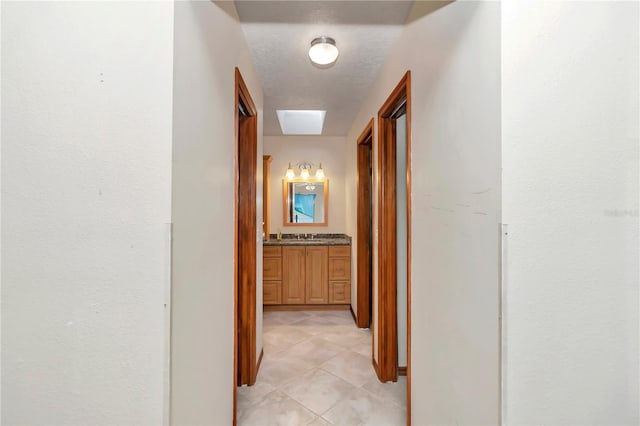 hall featuring a skylight, light tile patterned flooring, and a textured ceiling