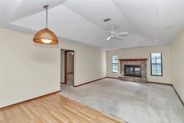 unfurnished living room featuring ceiling fan, a fireplace, light hardwood / wood-style floors, and a textured ceiling