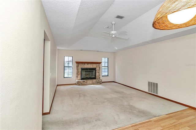 unfurnished living room featuring ceiling fan, a brick fireplace, light hardwood / wood-style floors, vaulted ceiling, and a textured ceiling