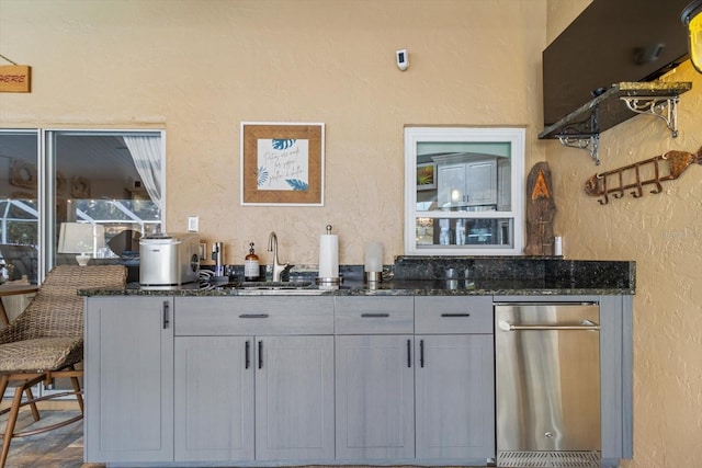 bar with gray cabinetry, dark stone countertops, and sink